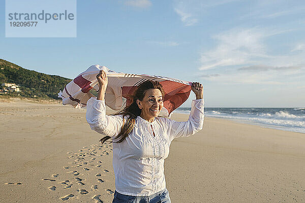 Glückliche ältere Frau mit Schal am Strand