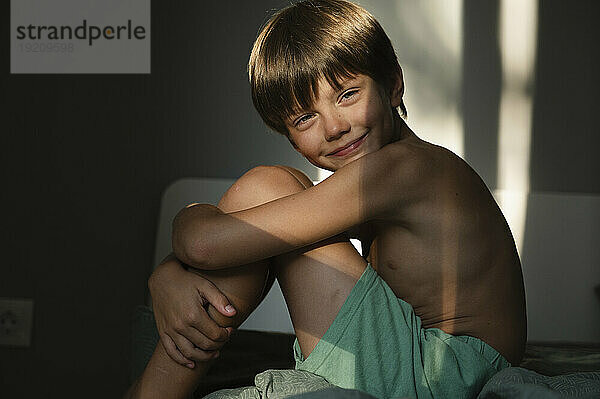 Cute boy sitting on bed at home