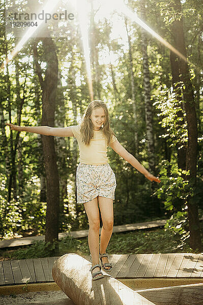 Lächelndes Mädchen balanciert auf Baumstamm im Park