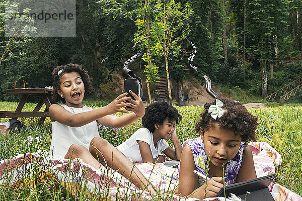 Mädchen klickt mit Smartphone auf Selfie neben Schwestern im Garten
