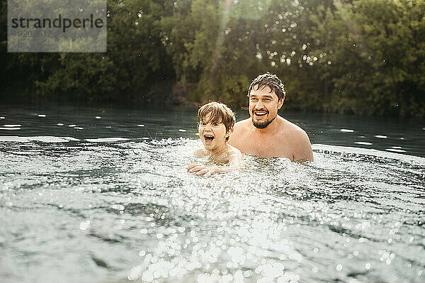 Glücklicher Vater und Sohn schwimmen an einem sonnigen Tag im Fluss