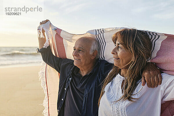 Glückliches älteres Paar mit Schal am Strand