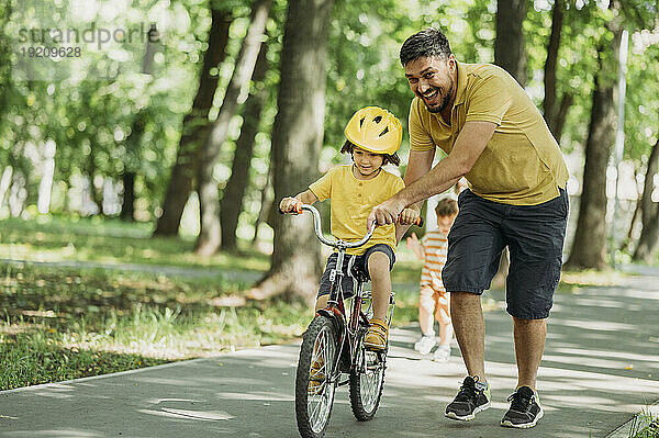 Glücklicher Vater hilft seinem Sohn beim Fahrradfahren auf dem Fußweg im Park