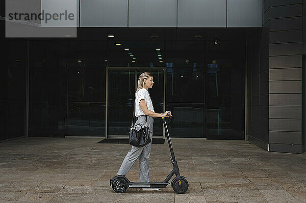 Geschäftsfrau läuft mit Elektroroller im Büropark