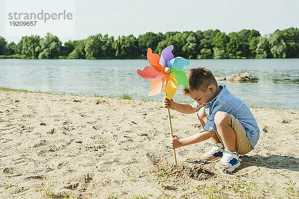 Junge spielt mit buntem Regenbogen-Windradspielzeug am Seeufer
