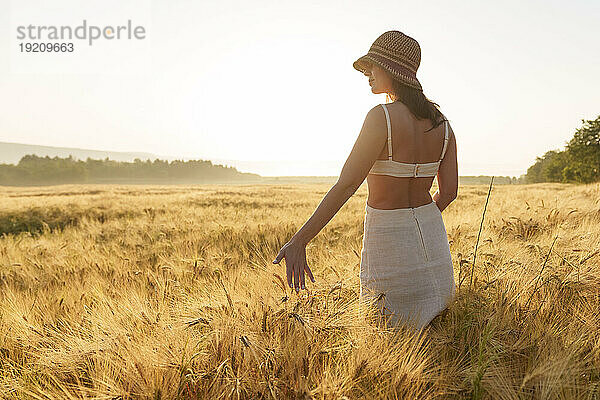 Frau mit Hut steht inmitten der Weizenernte im Feld