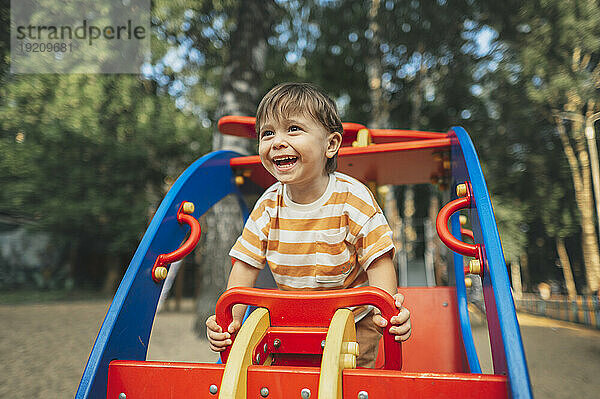 Lächelnder Junge sitzt auf Spielgeräten im Park
