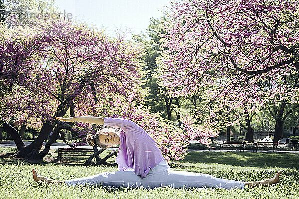 Teenager-Mädchen mit gespreizten Beinen praktiziert Yoga im blühenden Park