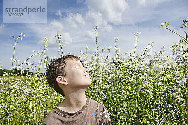Lächelnder Junge genießt Sonnenlicht im Rapsfeld