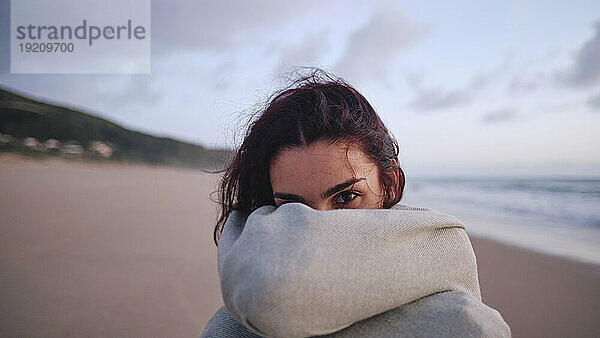 Junge Frau bedeckt Gesicht mit Decke am Strand