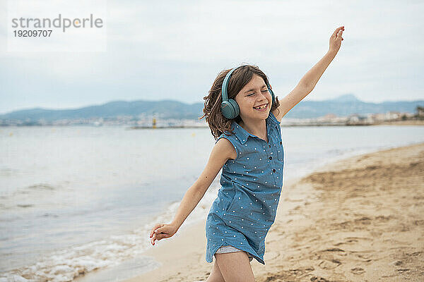 Fröhliches Mädchen mit kabellosen Kopfhörern genießt es am Strand