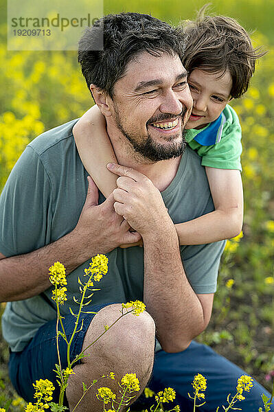 Glücklicher Sohn umarmt Vater auf gelbem Blumenfeld