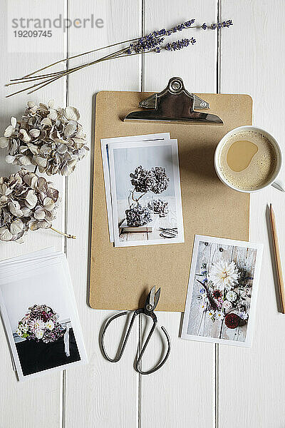 Tasse Kaffee  Klemmbrett  Trockenblumen und Fotos von Blumenarrangements auf weiß gestrichenem Holz