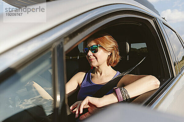 Lächelnde Frau sitzt an einem sonnigen Tag im Auto