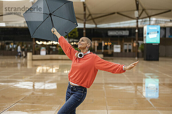 Sorglose Frau tanzt mit Regenschirm in der Stadt