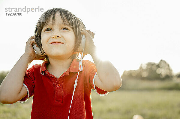 Lächelnder Junge mit Kopfhörern  der an einem sonnigen Tag Musik hört