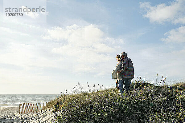 Älteres Paar steht an einem sonnigen Tag zusammen inmitten von Pflanzen am Strand