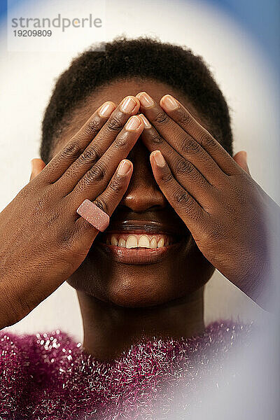 Happy young woman covering eyes against colored background