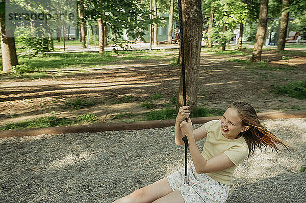 Cheerful girl swinging on swing at park