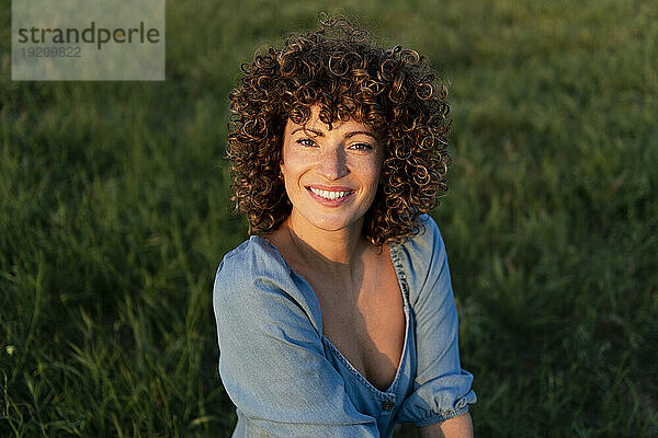 Smiling woman with curly hair crouching in meadow
