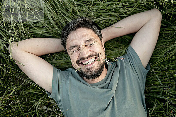 Happy man with beard lying on grass in field