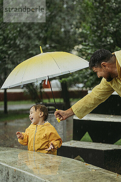 Vater hält Regenschirm für Sohn im Park