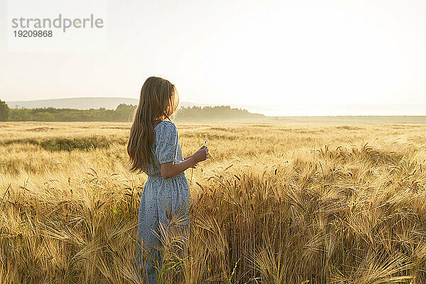 Mädchen mit langen Haaren steht bei Sonnenaufgang im Weizenfeld