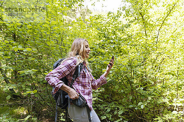 Lächelnder Wanderer nutzt Smartphone im Wald