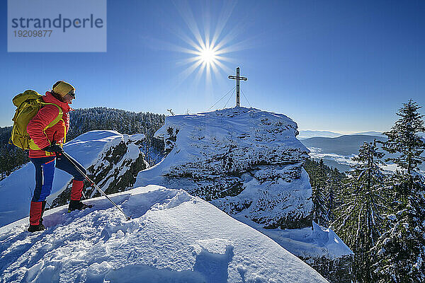 Woman in ski-wear hiking near summit cross on snow covered mountain