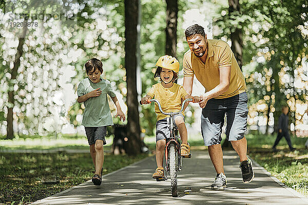 Glücklicher Vater hilft Sohn beim Fahrradfahren im Park