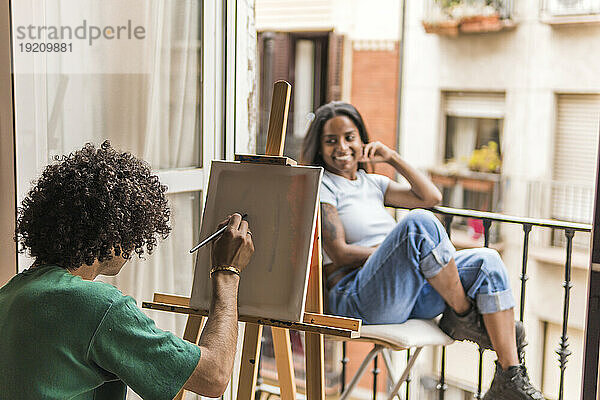 Freund malt auf Leinwand mit Freundin  die zu Hause posiert