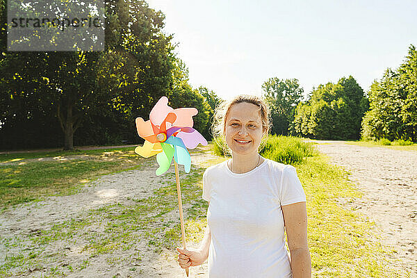 Lächelnde schwangere Frau hält Regenbogen-Windradspielzeug auf dem Feld