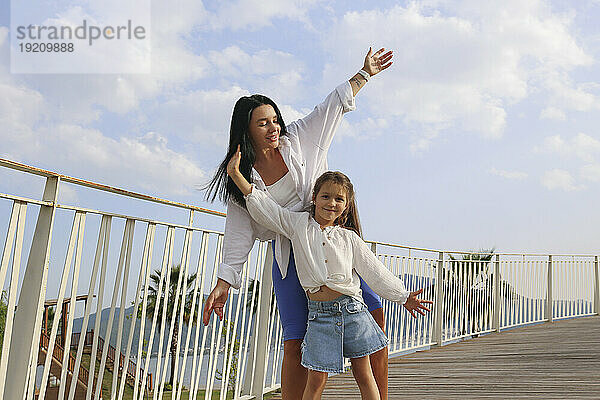 Glückliche Mutter und Tochter tanzen mit erhobenen Armen an einem sonnigen Tag