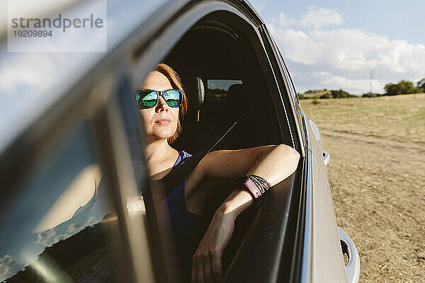 Nachdenkliche Frau sitzt an einem sonnigen Tag im Auto