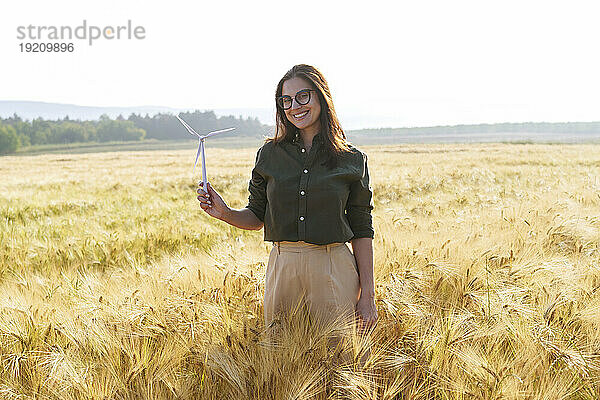 Lächelnder Agronom hält eine Modell-Windkraftanlage inmitten von Weizenpflanzen auf dem Feld