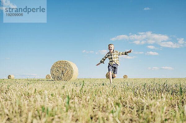 Happy boy running in field with haystacks