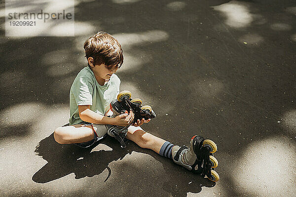 Junge zieht auf Fußweg sitzende Inline-Skates aus
