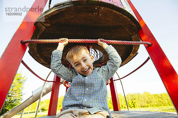 Fröhlicher Junge sitzt und hat Spaß auf dem Spielplatz