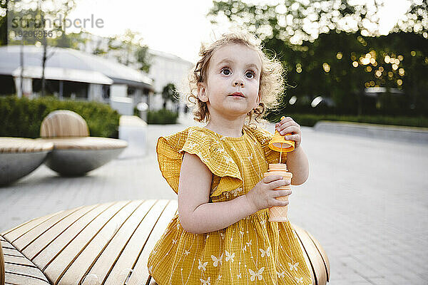 Nachdenkliches Mädchen im gelben Kleid mit Seifenblasenstab