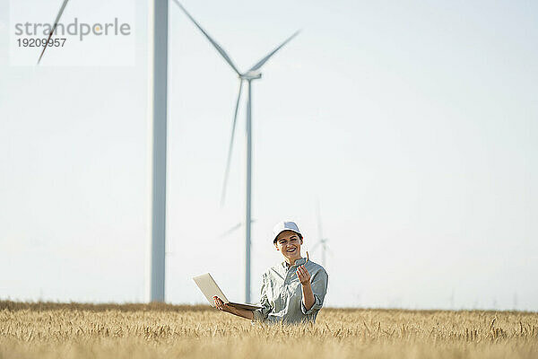 Glücklicher Bauer steht mit Laptop und untersucht das Weizenfeld an einem sonnigen Tag