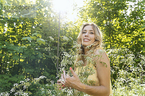 Smiling woman standing amidst flowers in forest