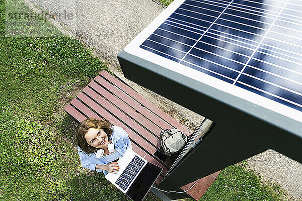Lächelnde Frau mit Laptop blickt auf Solarladestation