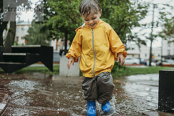 Happy boy splashing water in puddle at park