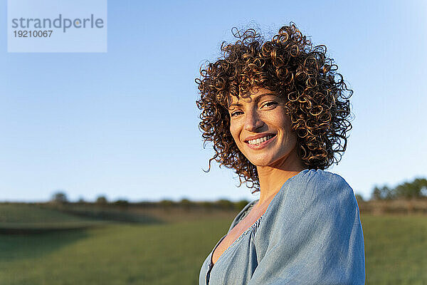 Glückliche Frau mit lockigem Haar bei Sonnenuntergang