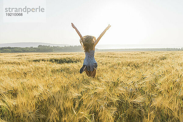 Mädchen mit ausgestreckten Armen springt im Weizenfeld