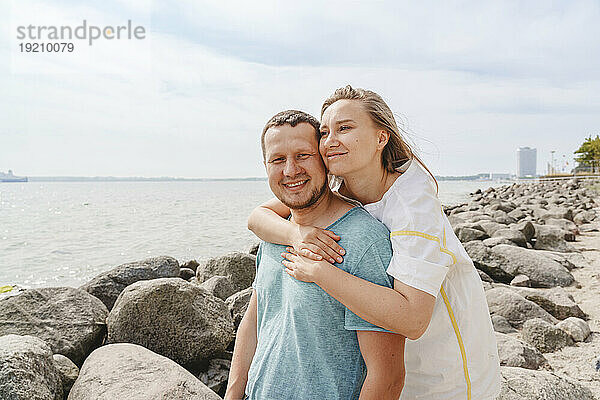 Lächelnde Frau umarmt Mann am Strand