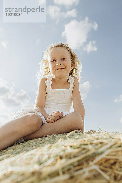 Lächelndes Mädchen  das an einem sonnigen Tag auf einem Strohballen sitzt