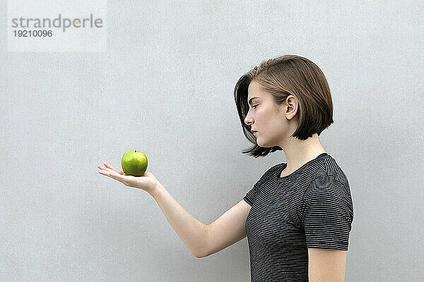 Teenager-Mädchen hält grünen Apfel vor grauem Hintergrund