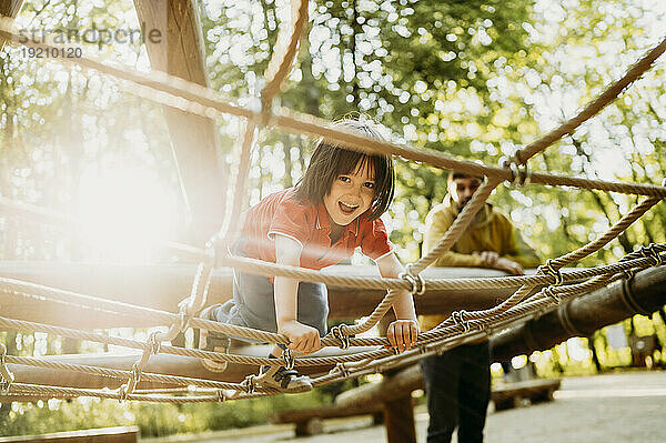 Lächelnder Junge  der im Klettergerüst am Seil spielt