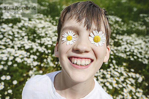 Happy boy with chamomile flowers over eyes